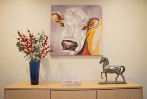 A cabinet top setting displaying a vase of flowers, a book and a chrome paperweight with a painting hanging above.