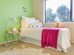 A HomeStaged kids bedroom with green walls and a white and pink bed.